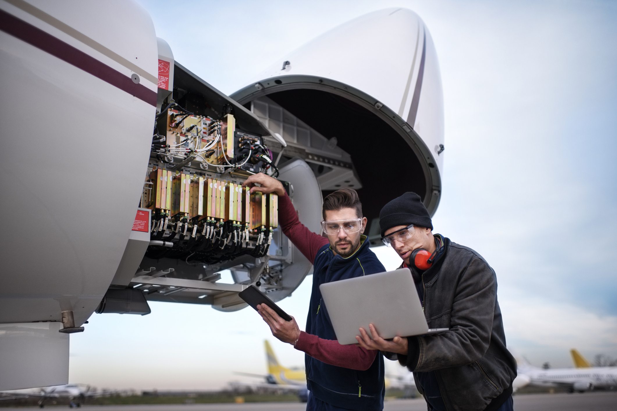 Technicians inspecting aircraft electronics at open nose cone